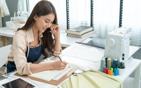 Asian tailor woman talking on phone with customer in tailoring atelier.